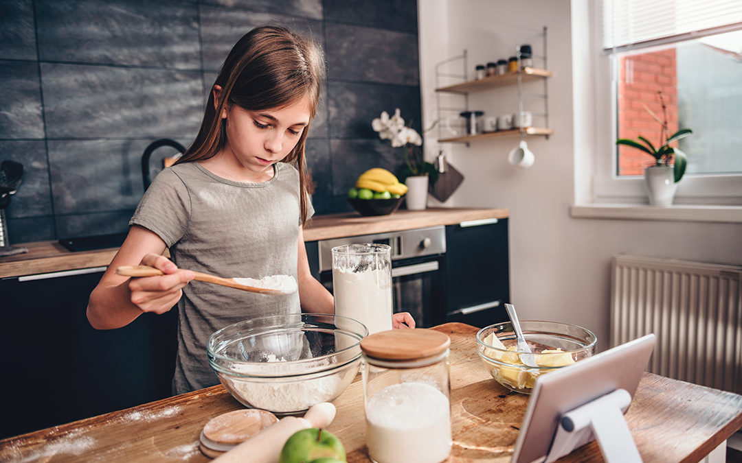 Girl performing example of algorithmic thinking while spooning flour into a bowl and following recipe in home kitchen