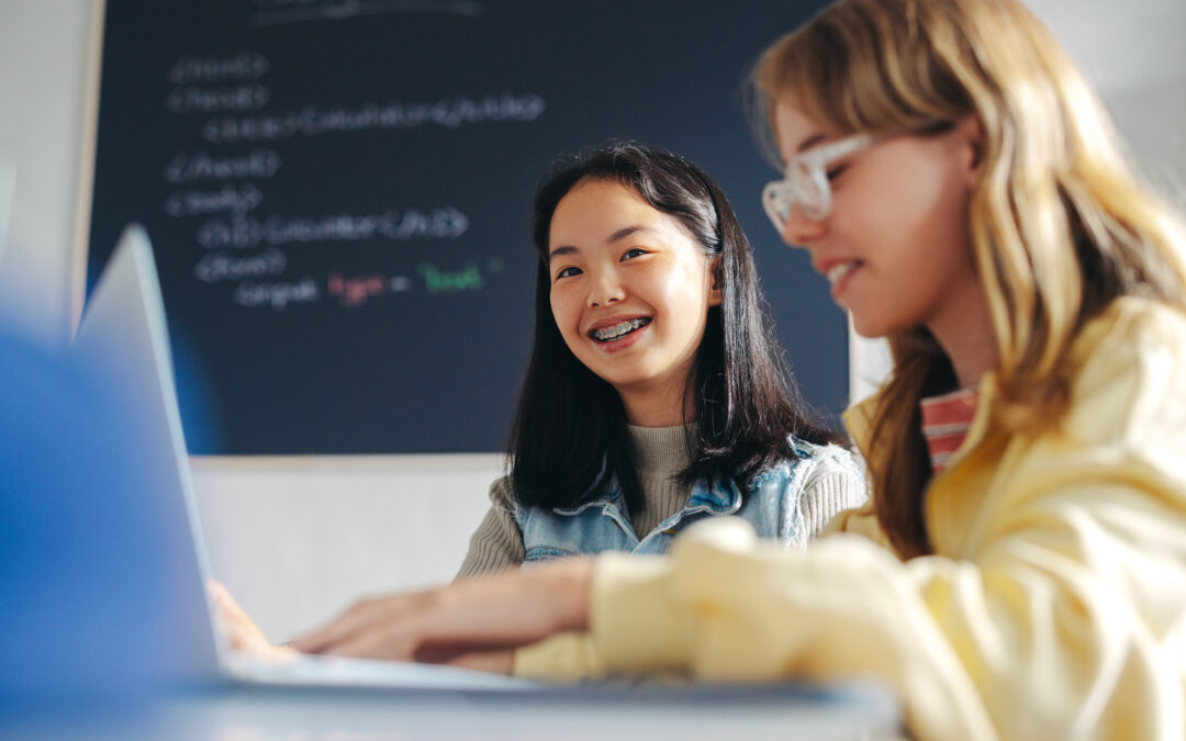 Two young female students thinking like programmers on a laptop in a classroom