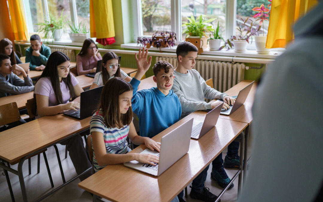Middle school digital literacy class with netiquette guidelines in place positively engaging in classroom culture, boy raising hand and smiling at teacher