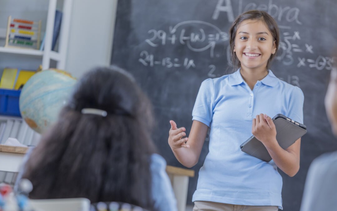Confident female student holding tablet giving presentation in math classroom to represent future readiness and digital literacy
