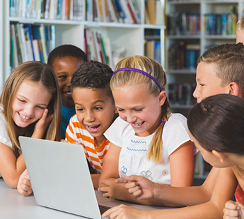 Elementary-age students smiling at laptop as they use AI safely to learn new topics in school