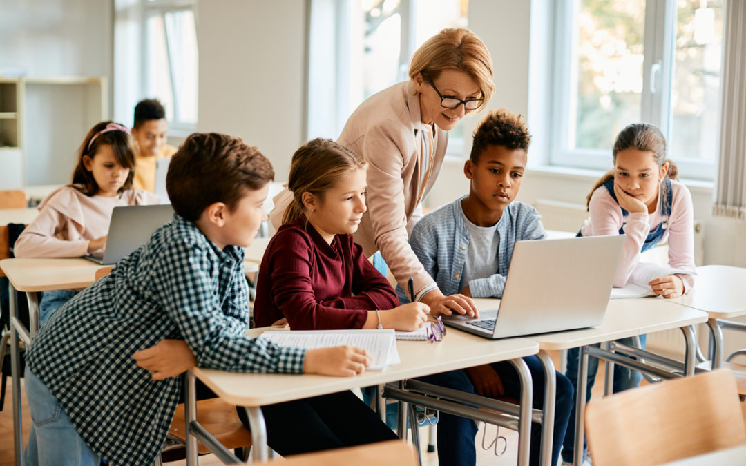 Teacher with students showing computer fundamentals on laptop